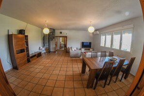 A spacious living area with a dining table, chairs, a TV, and a kitchen in the background. - Casa Dolly - Elegant Villa directly on the Tajo (VIILLAMANRIQUE DE TAJO)