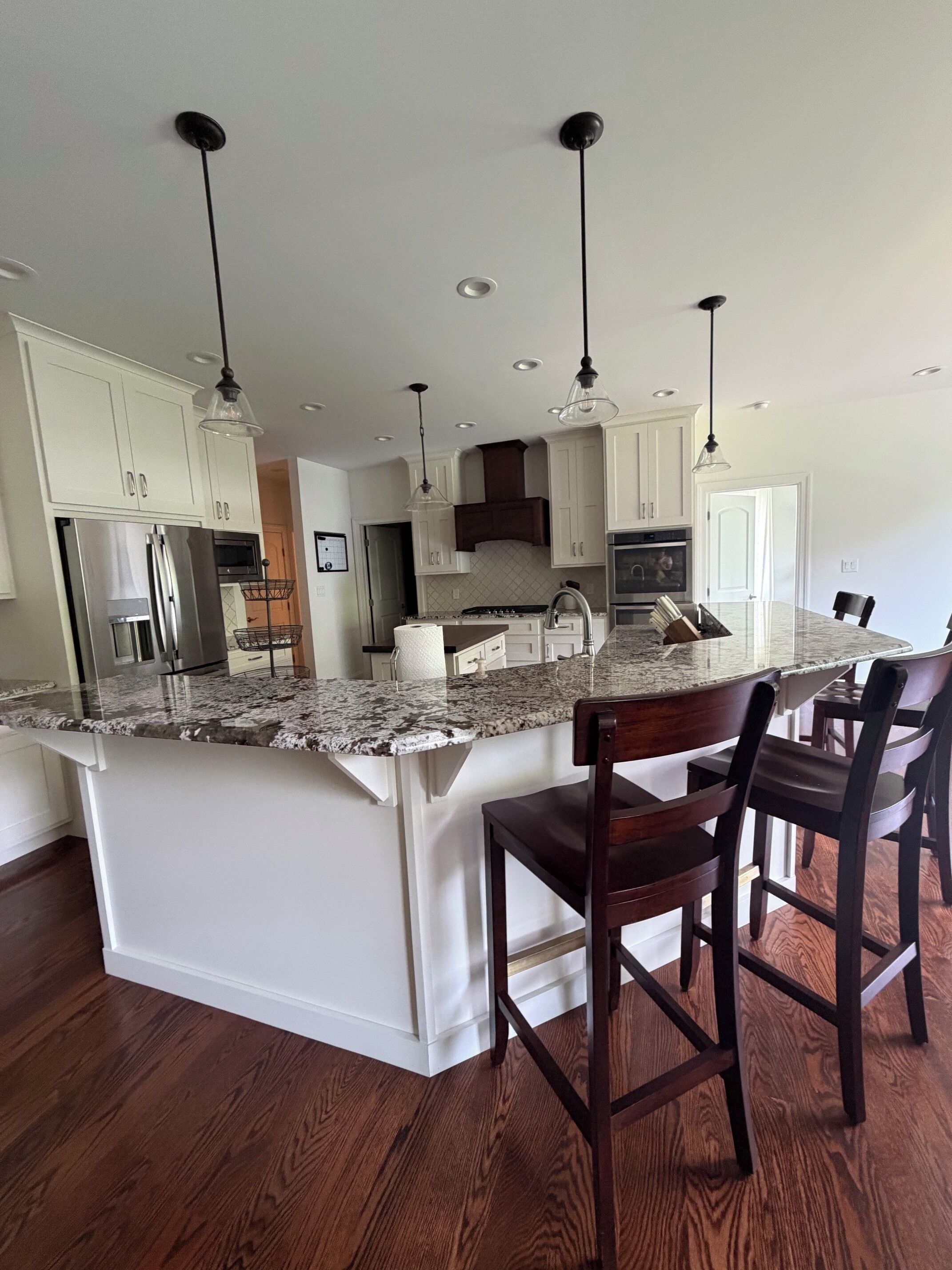 Cocina con una isla grande, armarios blancos, electrodomésticos de acero inoxidable y suelo de madera.