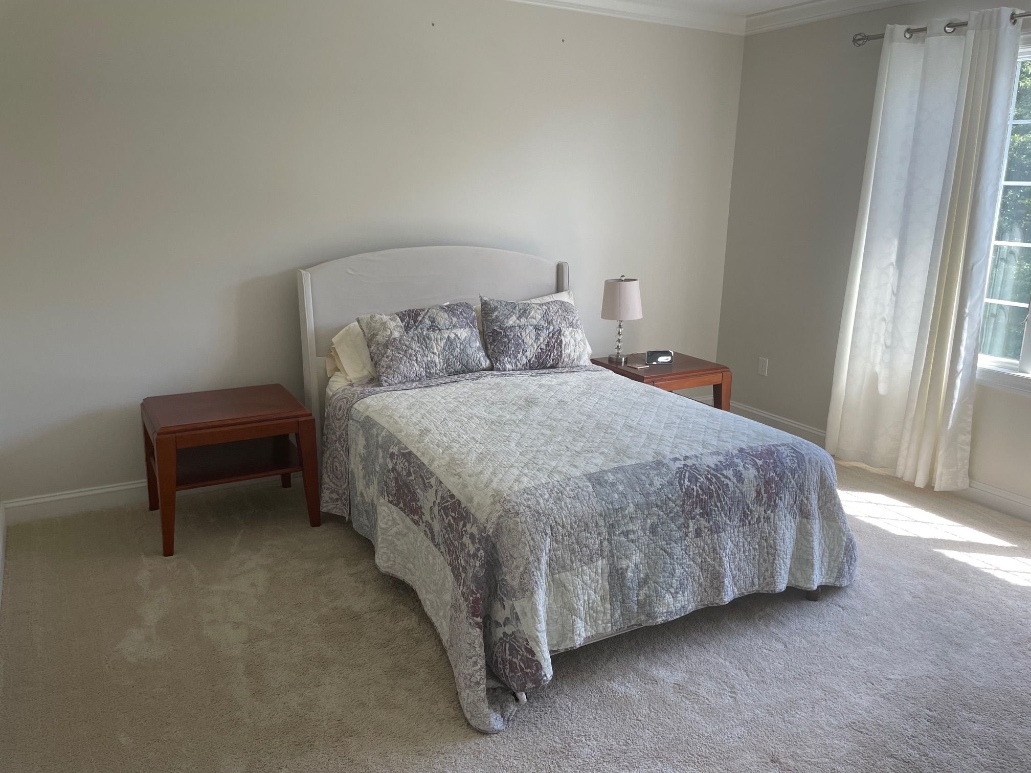 A bedroom with a bed, two nightstands, a lamp, and a window with curtains.