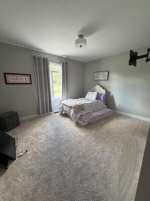 Une chambre à coucher avec un lit, une fenêtre avec des rideaux, un ventilateur de plafond et un téléviseur fixé au mur.