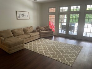 A living room with a sectional sofa, a patterned rug, and a door leading to an outdoor patio. - Tranquil luxurious 4-bedroom home on a scenic 2.5 ace lot, min. from Penn State. (Port Matilda)