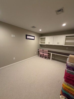 A room with carpeted flooring, a white ceiling with recessed lighting, a white cabinet unit, and a small table with two chairs.