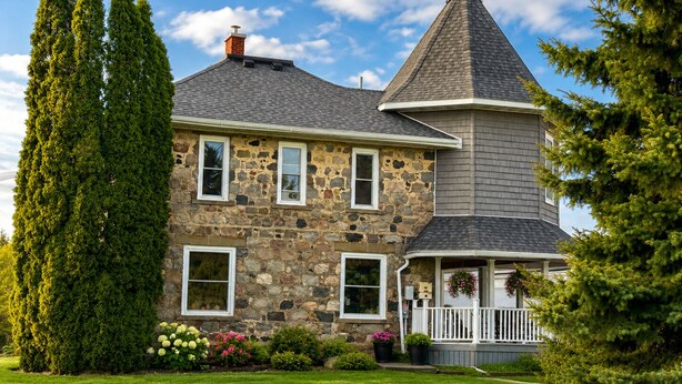 A stone house with a prominent tower, a front porch, and a well-maintained lawn.
