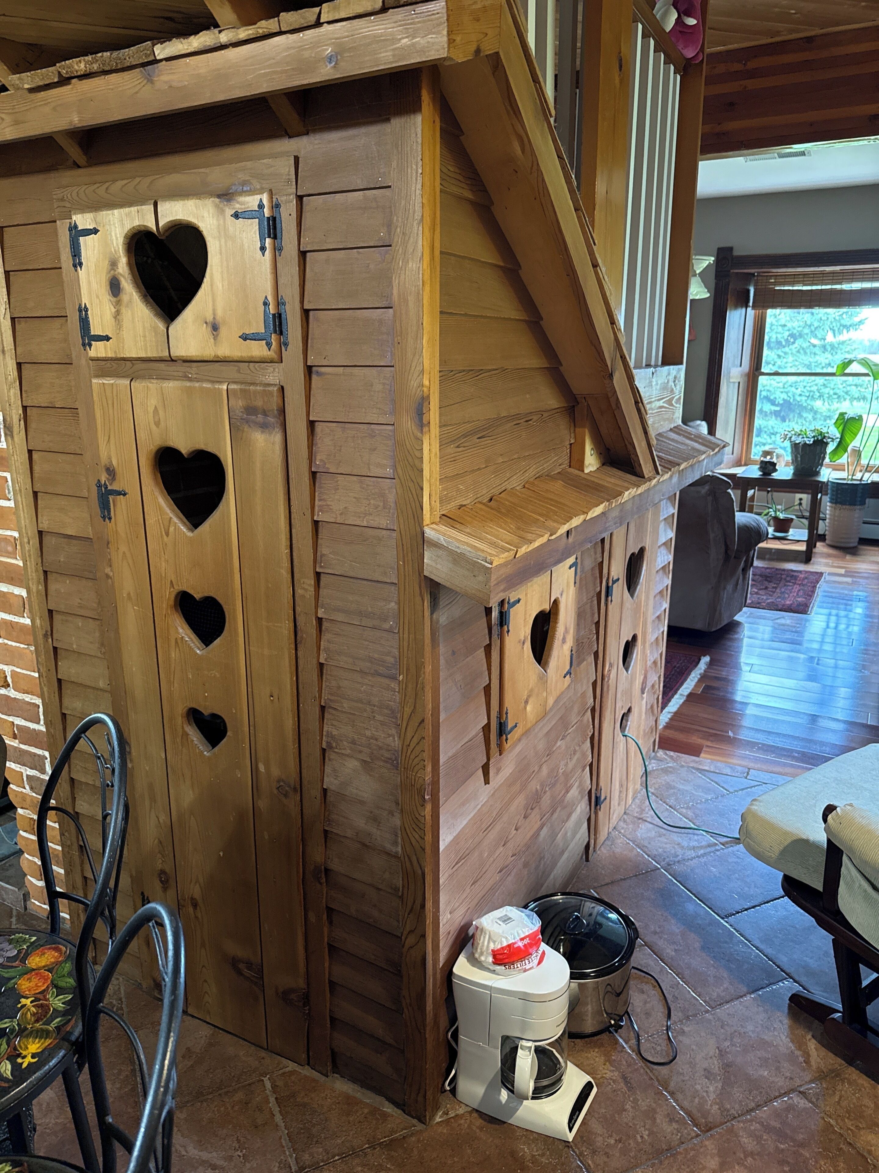 A wooden structure with heart-shaped cutouts, a staircase, and a coffee maker on the floor.