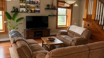 A living room with a sectional sofa, a flat-screen TV, wooden flooring, and a staircase.