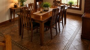 A dining area with a wooden table and chairs, a chandelier, and a view of the outdoors through a large window.