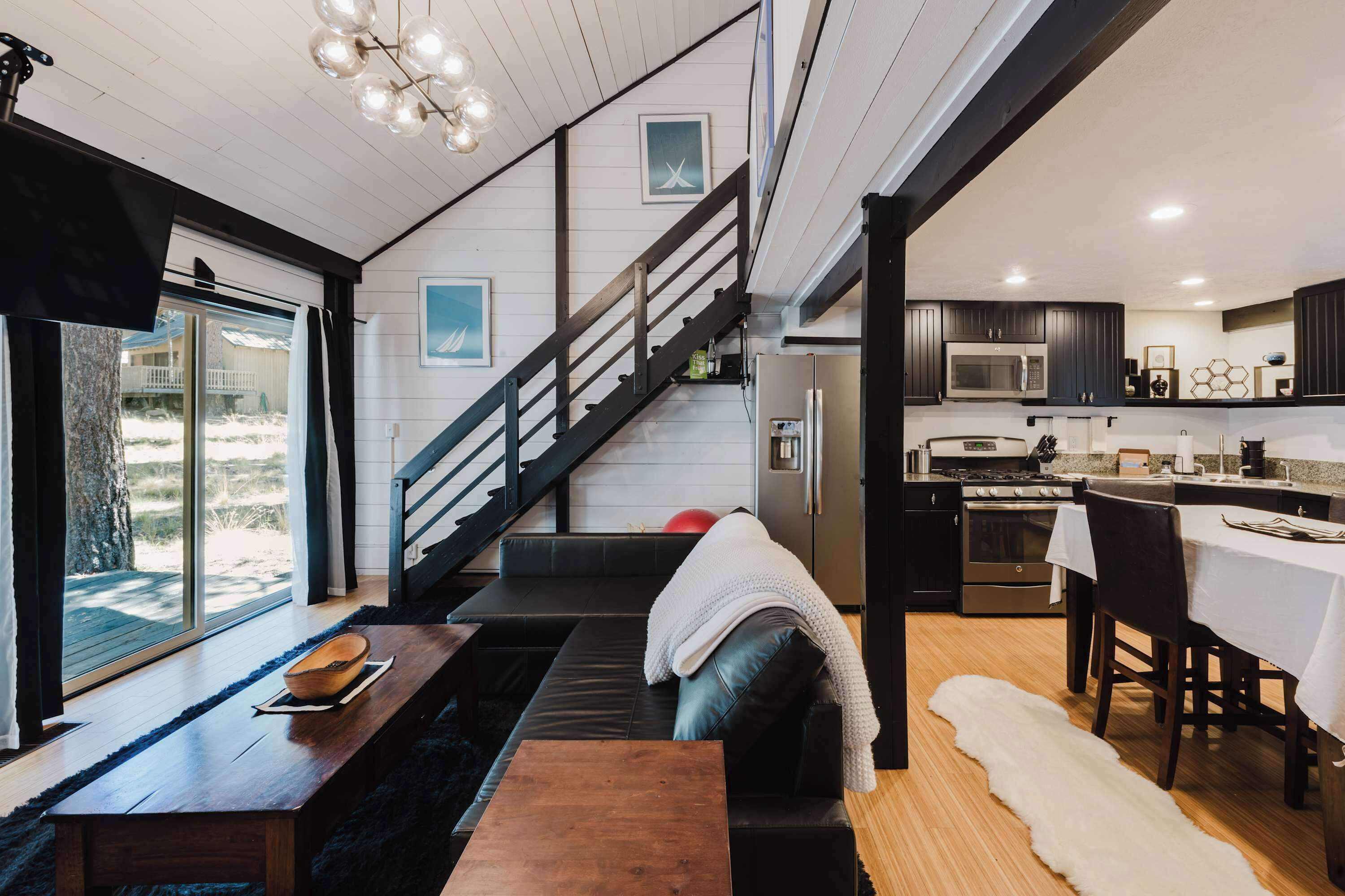 Et moderne interiør med en trappe, der fører til en balkon, et køkken med mørke skabe, og et siddeområde med sofa og sofabord.