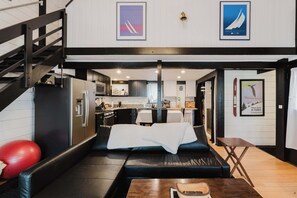A modern interior with a black leather sofa, a wooden coffee table, and a kitchen area in the background. - Cozy Sunriver Retreat - SHARC Passes, Bike and BBQ (Sunriver)