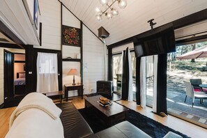 A modern living room with a fireplace, large windows, and a view of the outdoors. - Cozy Sunriver Retreat - SHARC Passes, Bike and BBQ (Sunriver)