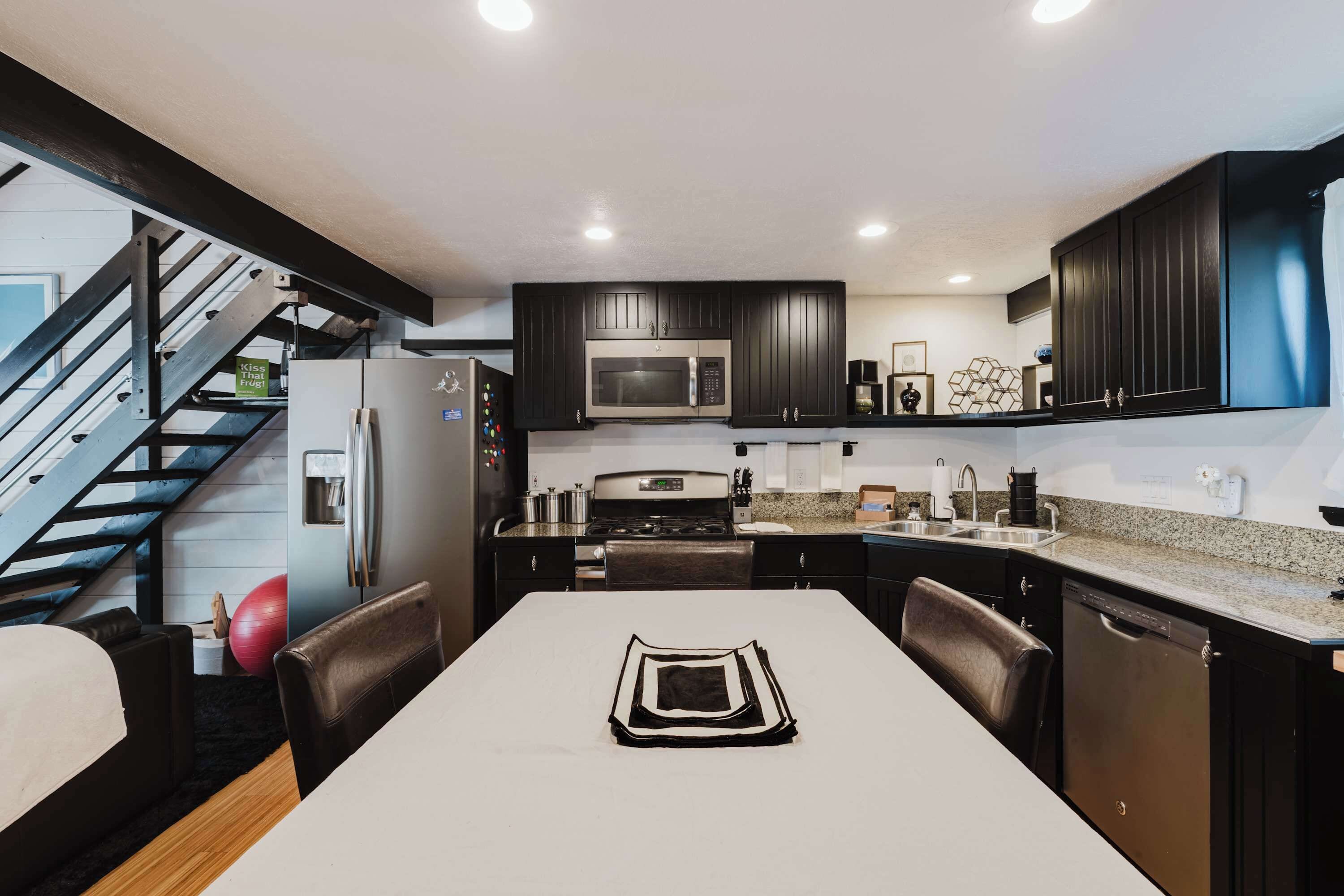 A modern kitchen with dark cabinetry, a stainless steel refrigerator, a microwave, and a gas stove. There is a dining table with chairs and a red exercise ball.