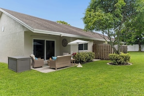 A residential property with a covered patio, outdoor furniture, and a well-maintained lawn.