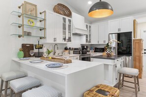 A modern kitchen with white cabinetry, a central island, bar stools, and a hanging light fixture.