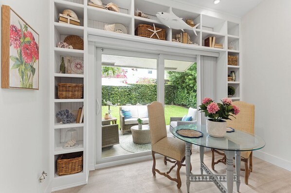 A room with a glass table, wicker chairs, and a view of a garden through a sliding door.
