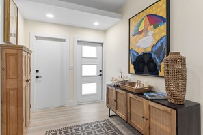 A hallway with a wooden cabinet, a console table with wicker baskets, a framed painting, and a patterned rug.