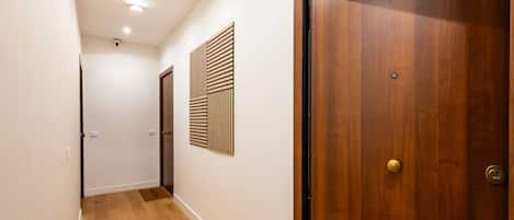 A hallway with wooden flooring, a wooden door, and a wall-mounted panel.