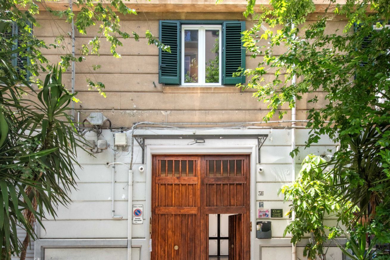 A building with a large wooden door, a window with green shutters, and a sign indicating a no parking zone.