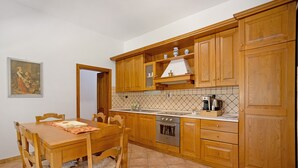A kitchen with wooden cabinets, a tiled backsplash, a stove, and a dining table with chairs. - Holiday Home 'Appartamento 3' with Shared Garden, Wi-Fi and Air Conditioning (Montiano)