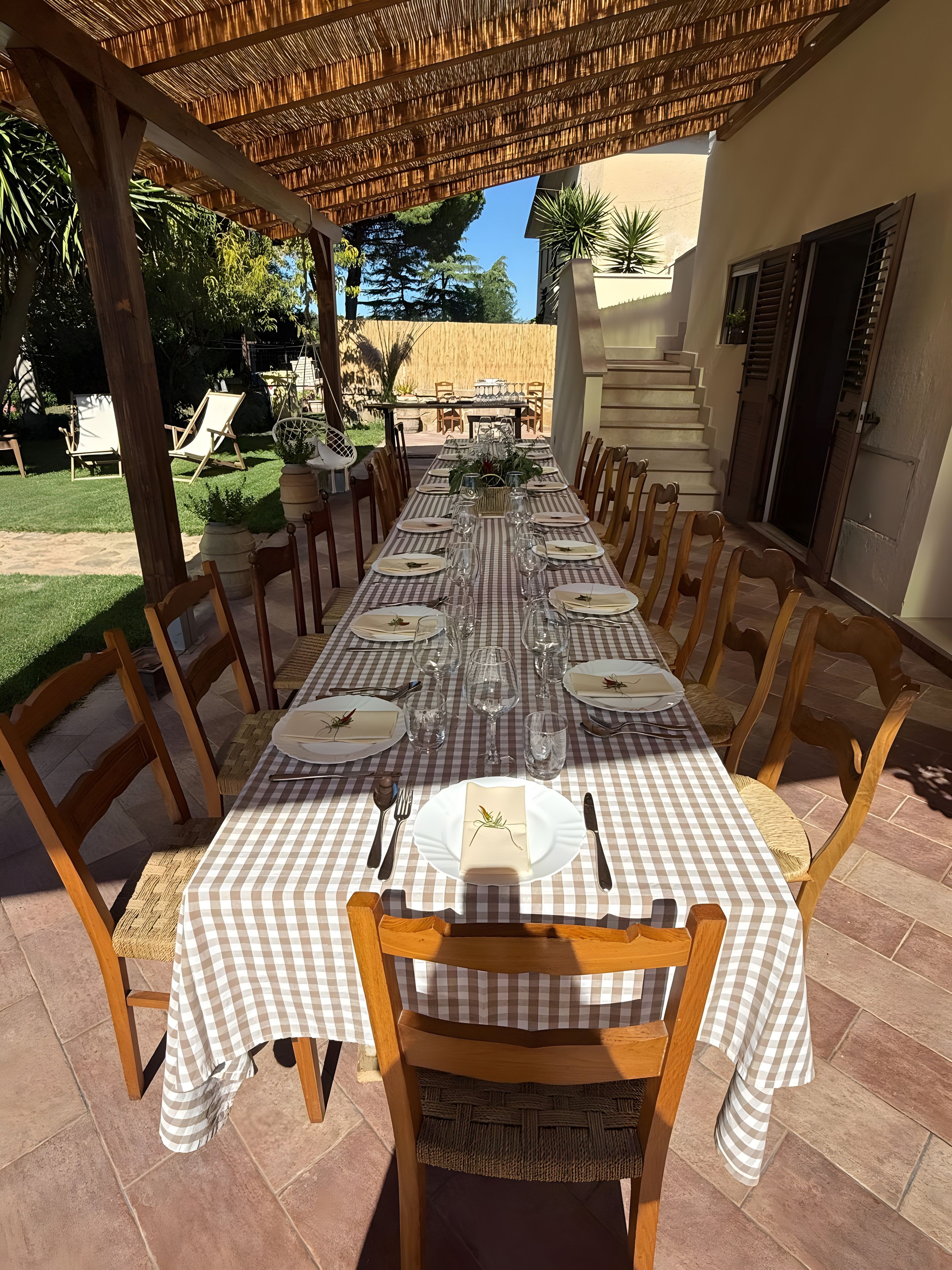Un espace extérieur abrité, aménag é pour les repas, avec une table recouverte d’une nappe à carreaux, des chaises en bois et une vue sur le jardin.