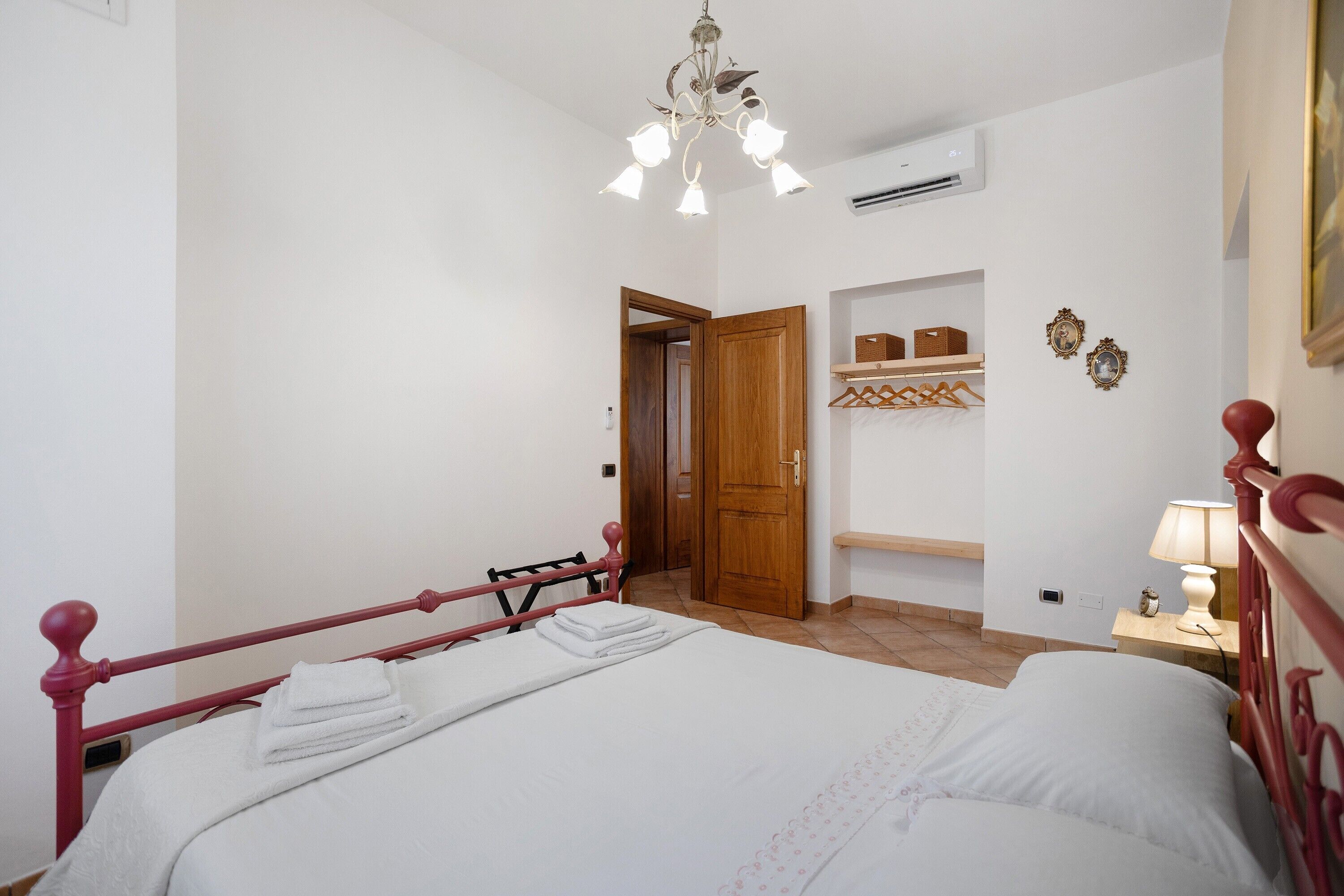 A bedroom with a bed, a wooden door, a shelf with baskets, and a wall-mounted air conditioner.