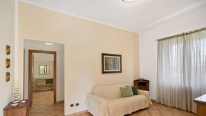 A living room with a beige sofa, a wooden cabinet, a framed picture on the wall, and a window with curtains. - Holiday Home 'Appartamento 3' with Shared Garden, Wi-Fi and Air Conditioning (Montiano)