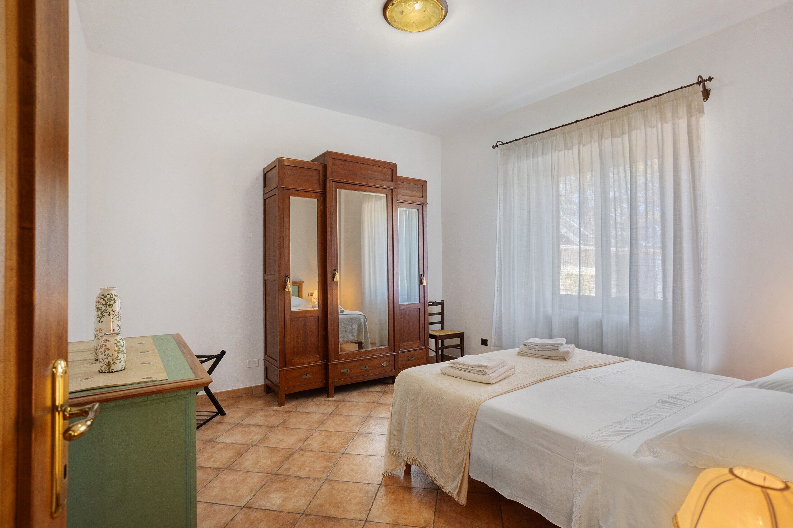 Una camera d'albergo con un letto, un armadio in legno, una scrivania con una sedia e una finestra con tende.