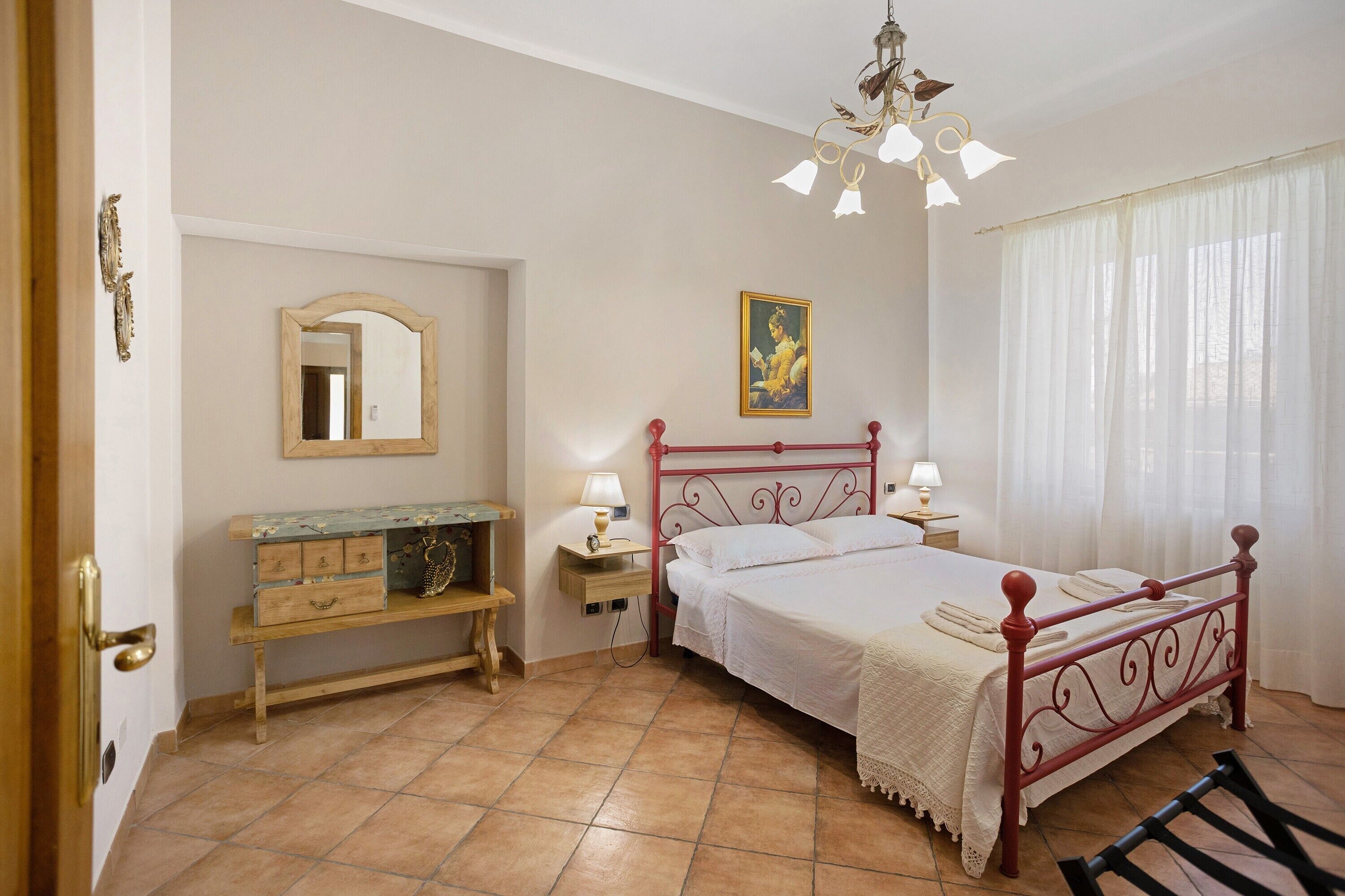 A bedroom with a bed, bedside tables, a dresser, a mirror, a painting, and a chandelier.