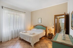 Ein Hotelzimmer mit einem Bett, einem Nachttisch, einer Lampe, einem gerahmten Bild und einer Vase auf einem Tisch.