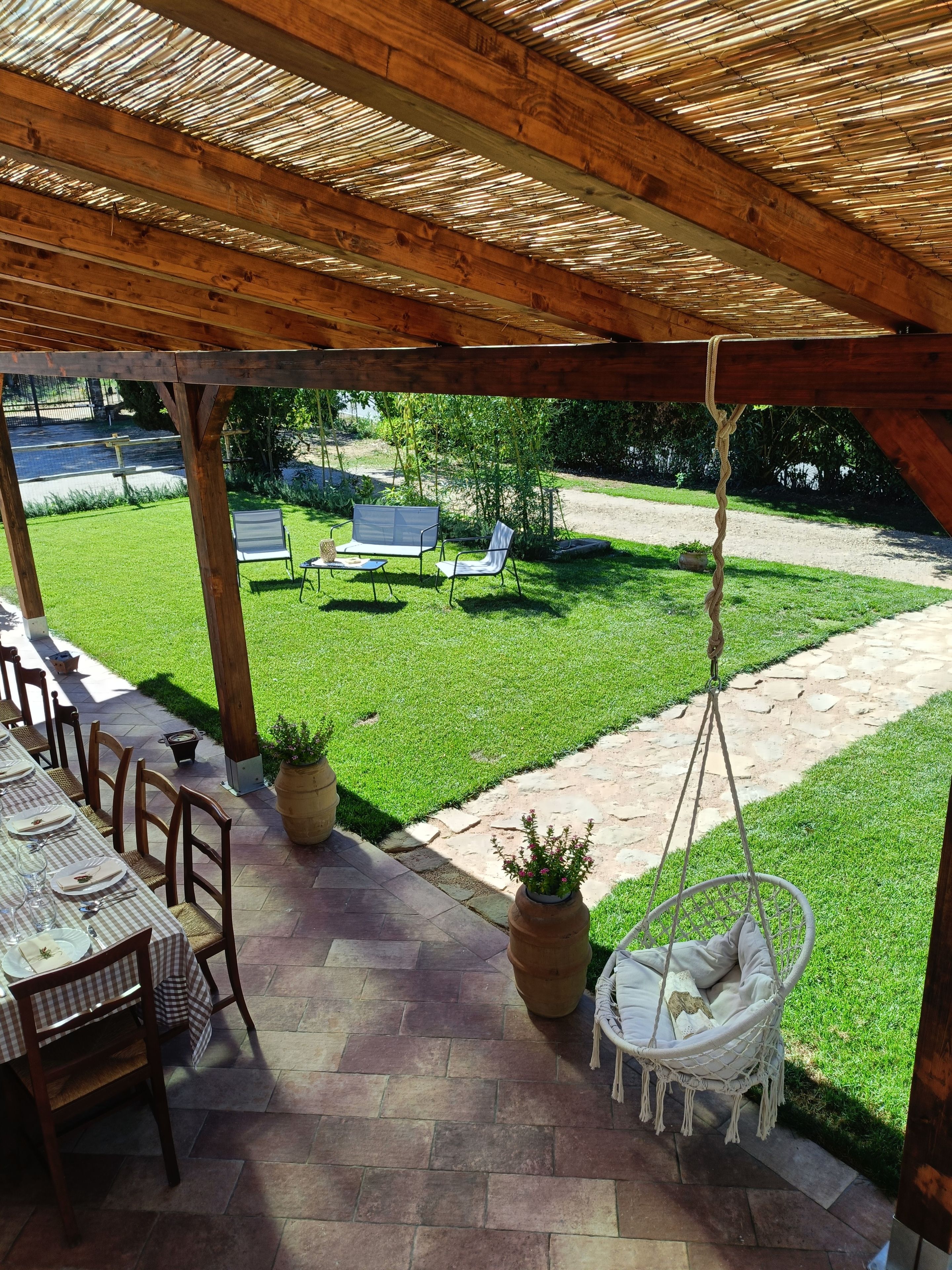 An outdoor patio with a covered seating area, a hanging chair, and a table set for dining.