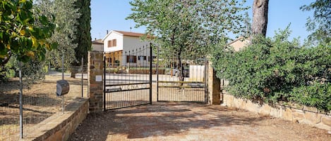 A gated entrance to a property with a stone wall, a metal gate, and a clear sky.