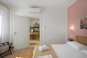 A hotel room with a bed, a desk, a chair, a small table, a painting, and a kitchen visible through an open door. - Apartment '2' with Shared Garden, Wi-Fi and Air Conditioning (Montiano)