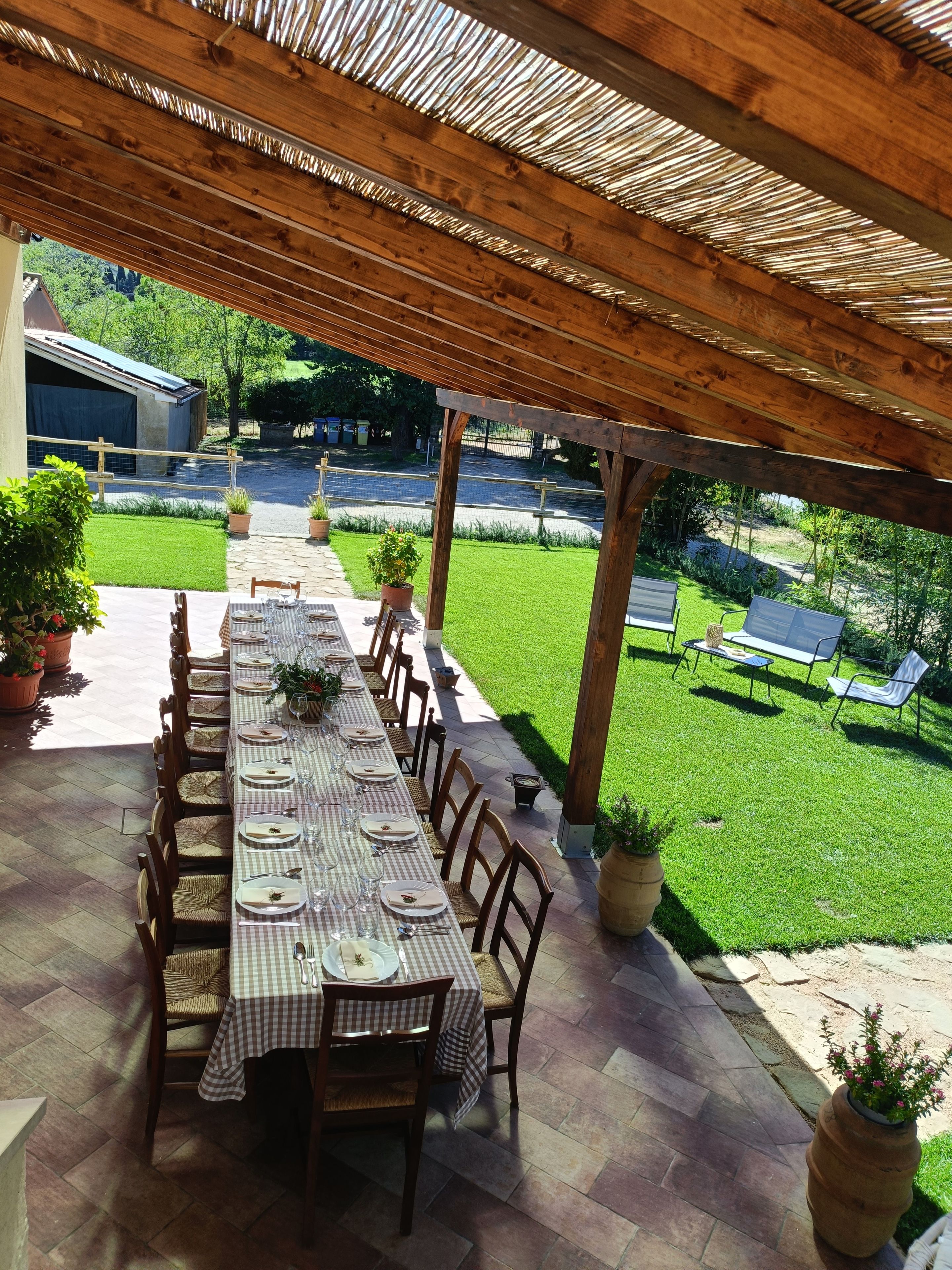 Zona pranzo all'aperto con un tavolo lungo apparecchiato per un pasto, circondato da sedie.