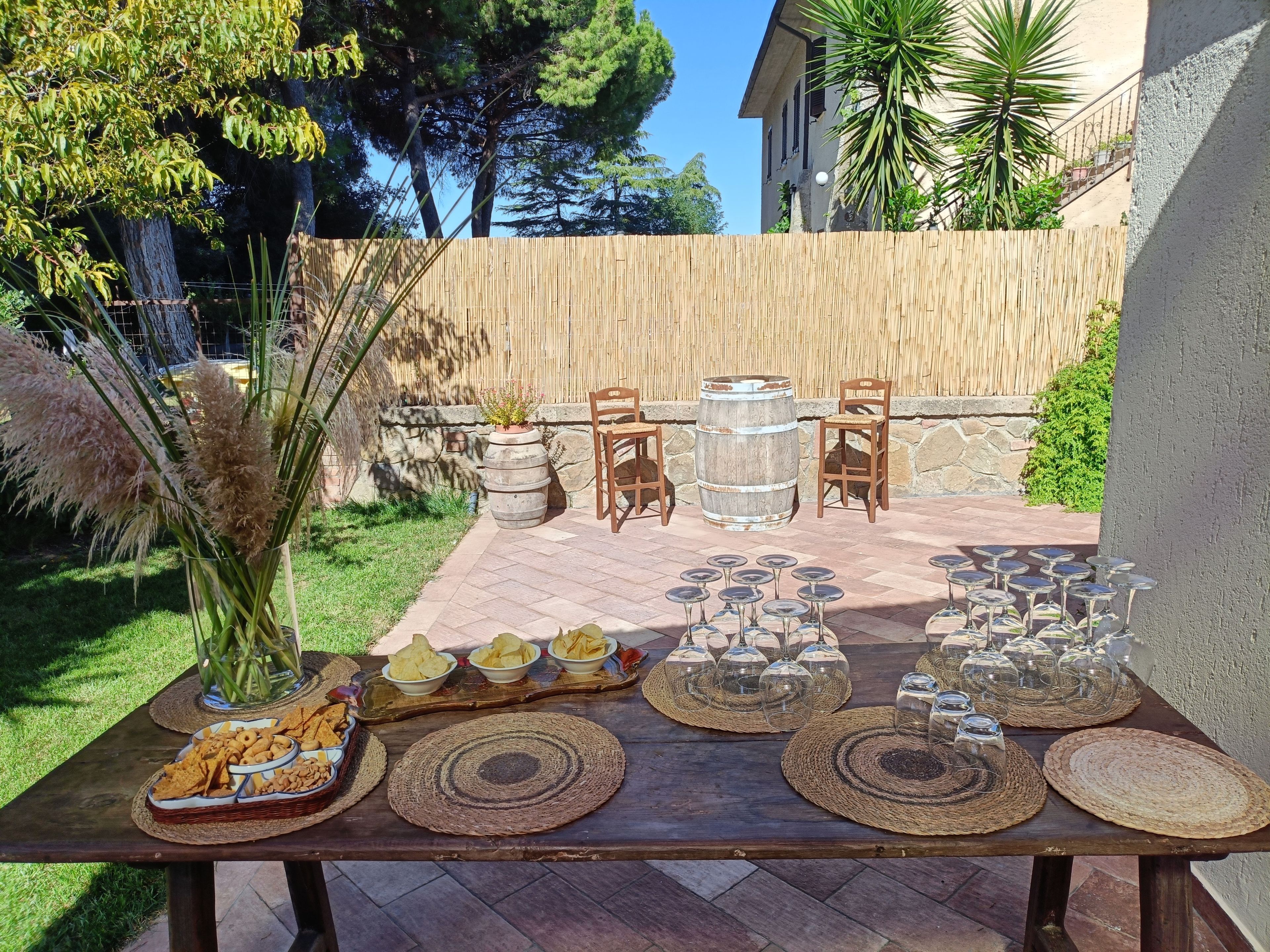 An outdoor patio with a wooden table set for a meal, surrounded by chairs and a decorative backdrop.