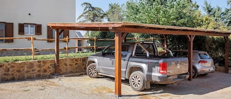 A gravel parking area with a wooden shelter and a vehicle.