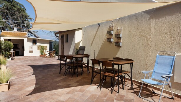 Un'area patio esterna con tavolo e sedie, un ombrellone e vista su un edificio sullo sfondo.