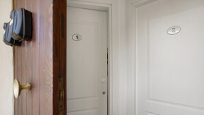 L'ingresso di una camera d'albergo, con una porta numerata, un campanello in ottone e un appendiabiti con una borsa.