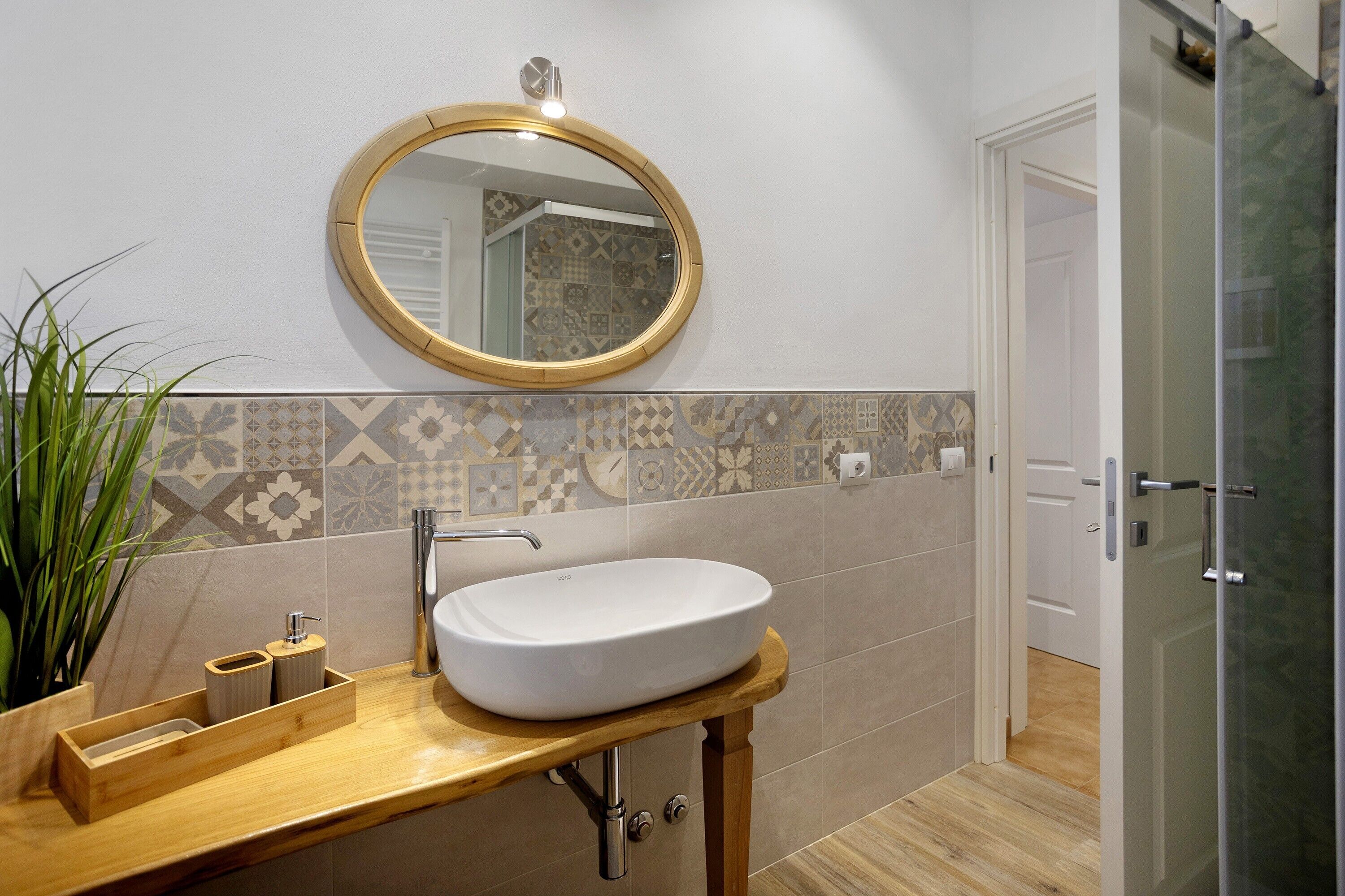 Une salle de bain avec un miroir rond, un lavabo blanc et un mur recouvert de carreaux à motifs.