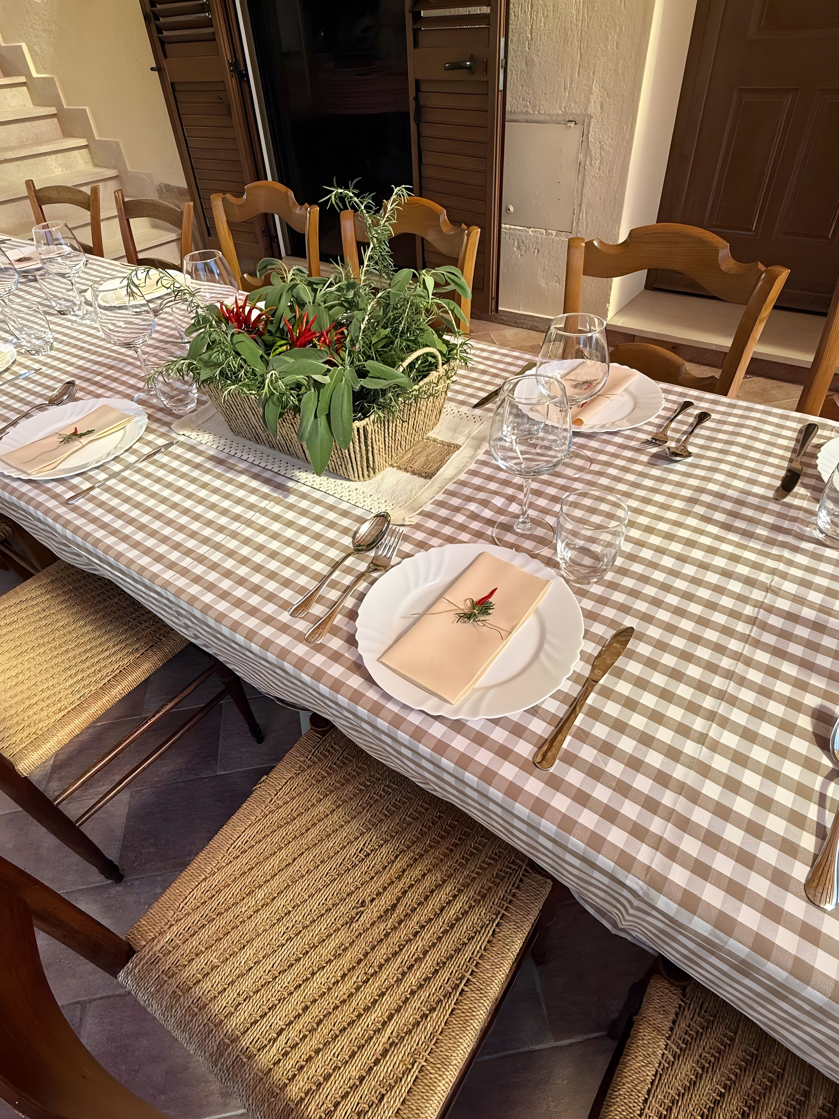 Una larga mesa de comedor dispuesta con mantel a cuadros, platos blancos y cubertería dorada.