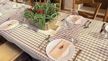 Een lange eettafel, gedekt met een geruit tafelkleed, witte borden en gouden bestek.