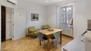 Una stanza piccola e luminosa con un tavolo di legno, due sedie, un termosifone e una finestra con tende leggere.