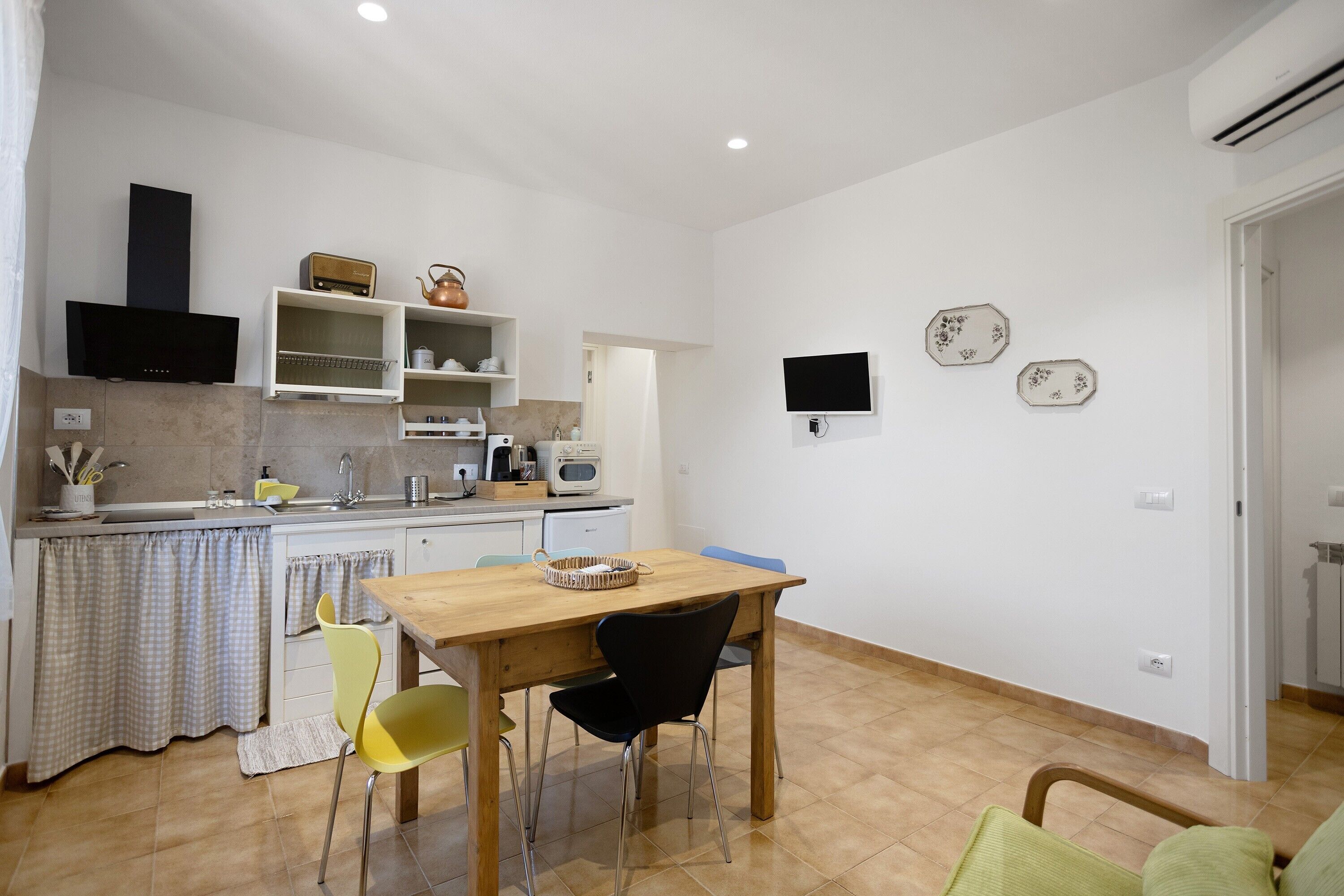 A compact kitchen with a dining area, a TV mounted on the wall, and a small table with chairs.