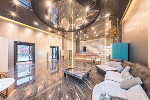 A modern lobby with a marble floor, a reception desk, seating area with sofas, and a large mirror on the wall.