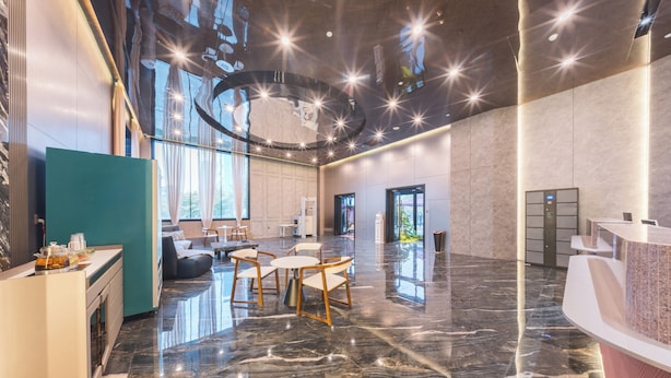 Un moderno vestíbulo de hotel con piso de mármol, una mesa de recepción y un área de descanso con una mesa y sillas.