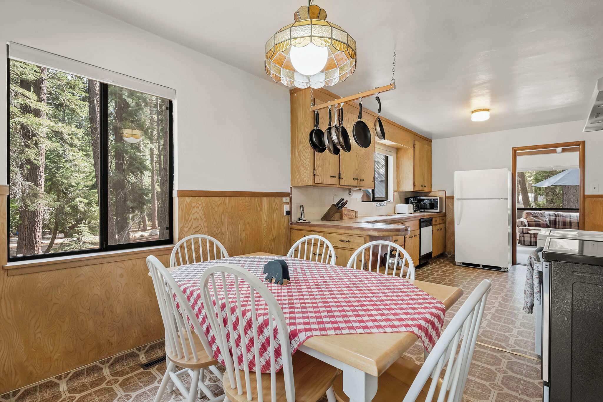 Cocina compacta con comedor, armarios de madera y vista al bosque a través de amplios ventanales.