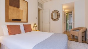 Een slaapkamer met een bed, kussens, een lamp, een spiegel en een stoel.