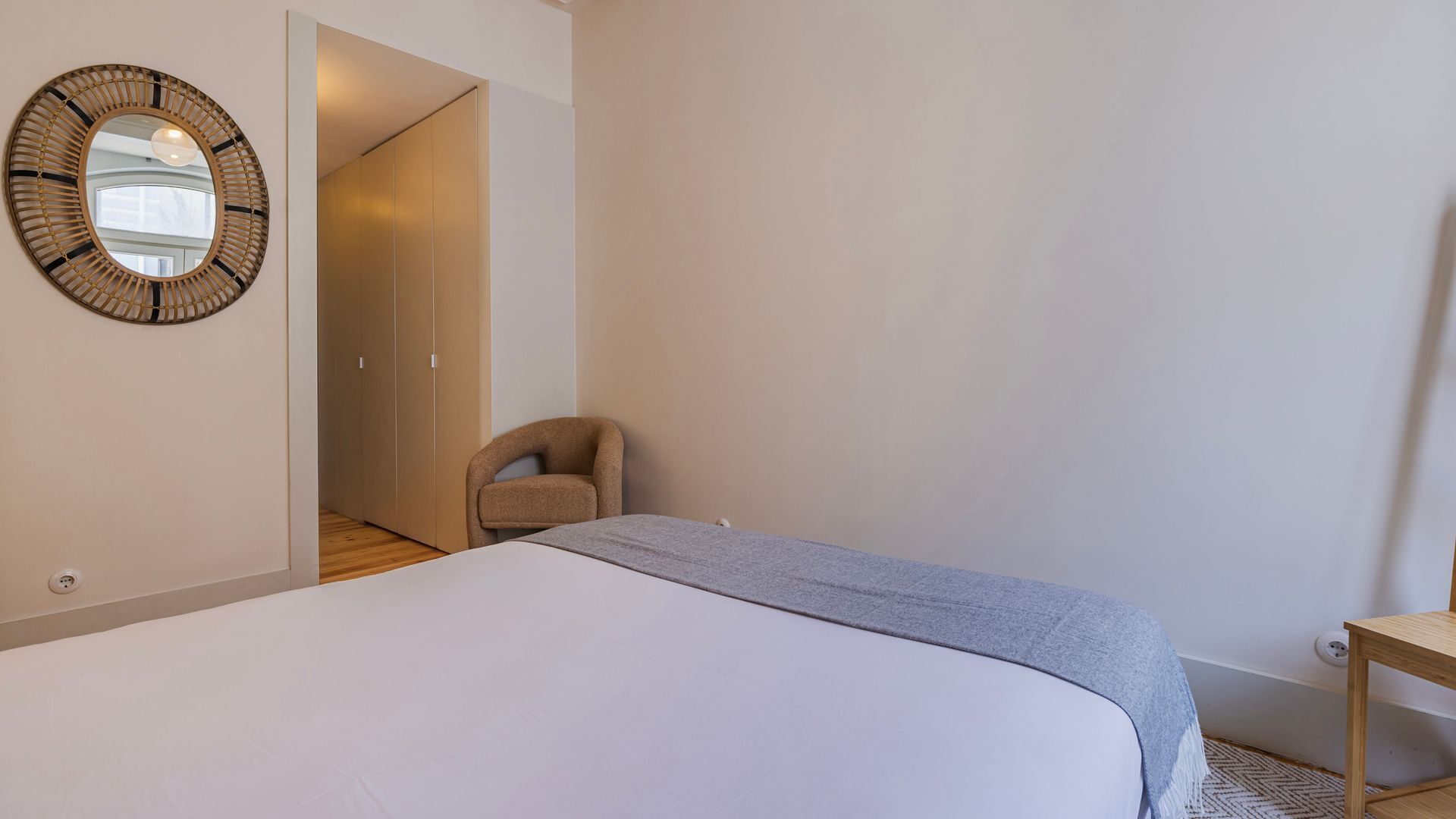 A bedroom with a bed, a chair, a mirror, and a wardrobe.