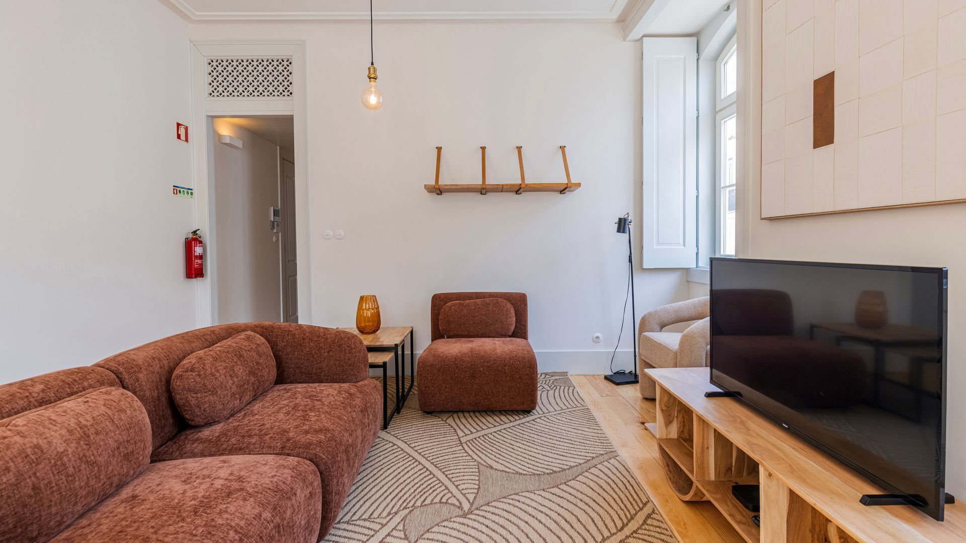 Un salon moderne avec un grand téléviseur à écran plat, un canapé marron, un fauteuil plus petit et un tapis à motifs.