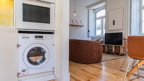 Ein moderner Waschraum mit einer Waschmaschine von Bosch, Holzboden, einem braunen Sofa und einem Fernseher im Hintergrund.
