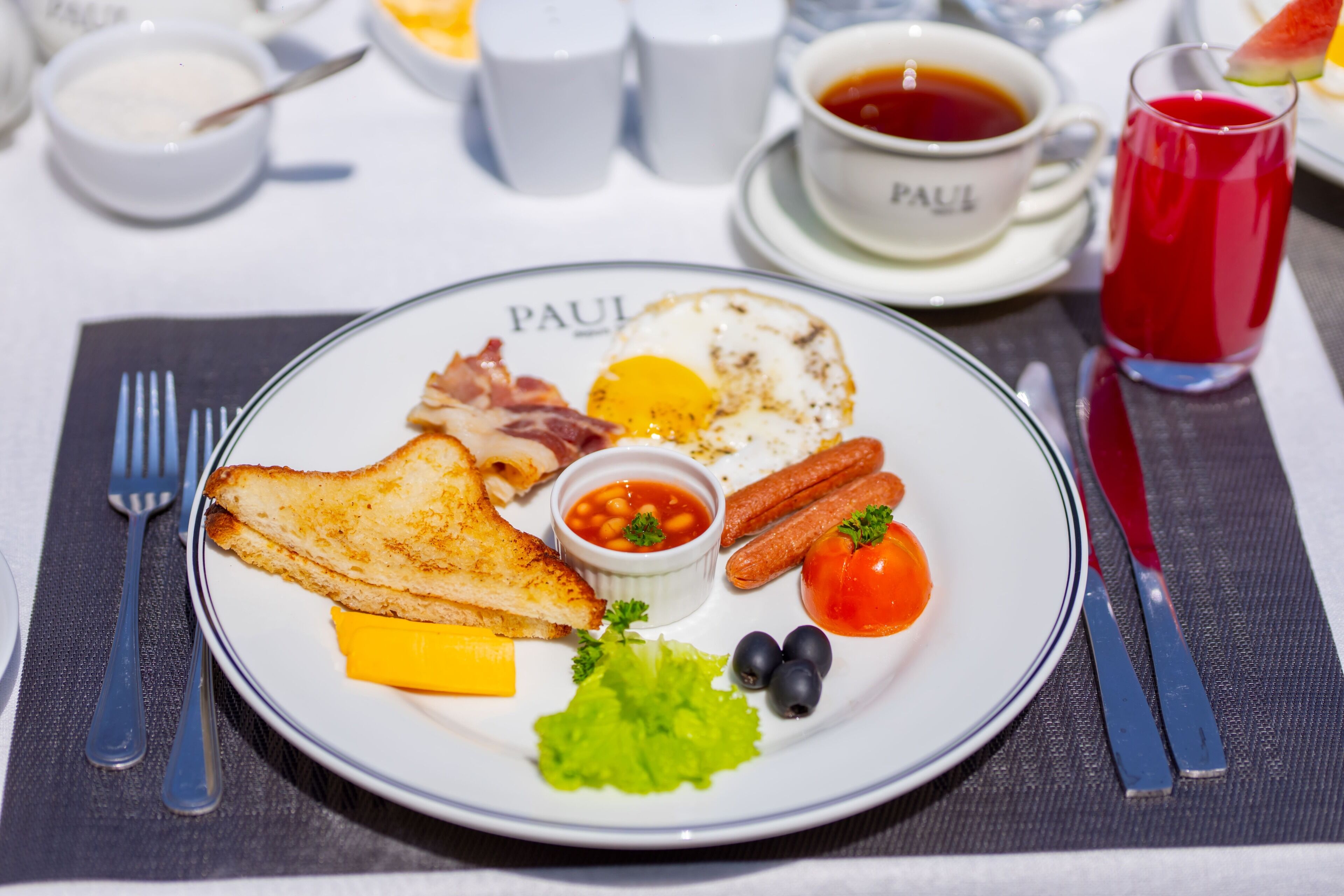 A breakfast plate with toast, eggs, bacon, tomatoes, and a small bowl of beans.