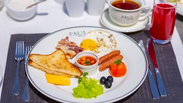 A breakfast plate with toast, eggs, bacon, tomatoes, and a small bowl of beans.