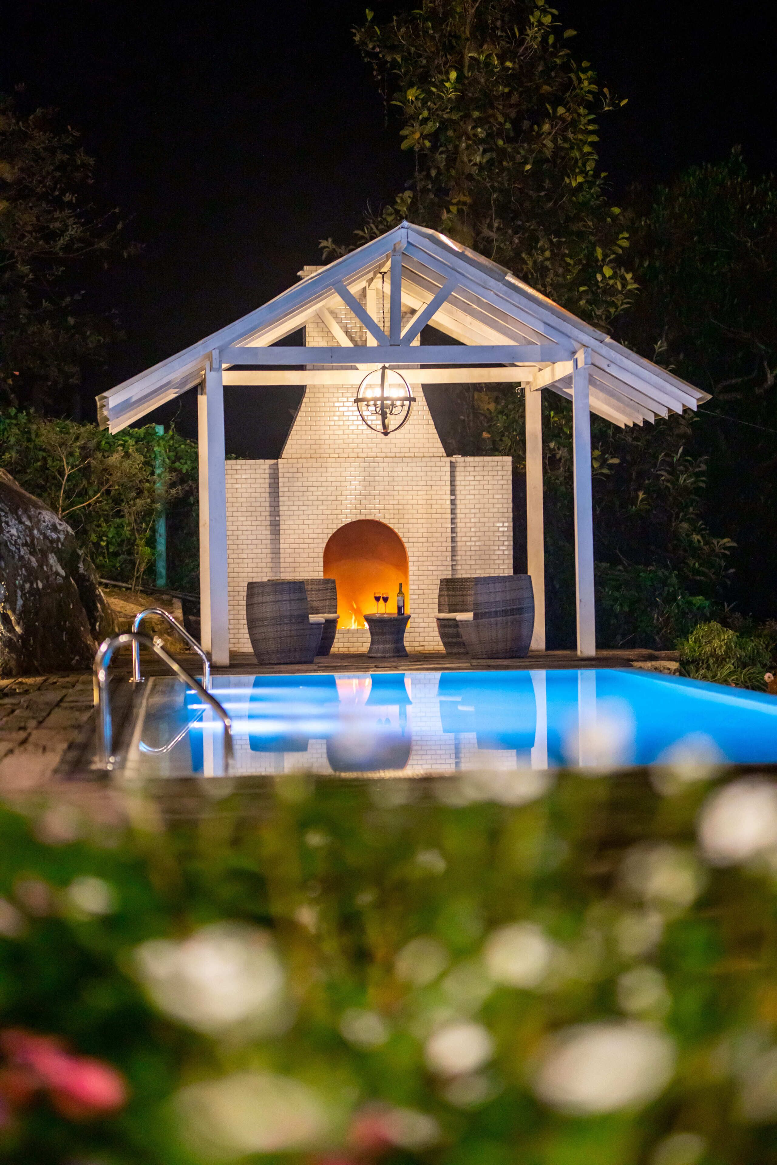 A pool area with a covered seating area and a fireplace.